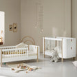 A beautifully styled nursery featuring an Oliver Furniture cot and junior bed in a Scandinavian-inspired design. The furniture is crafted from white and natural wood, with soft neutral tones creating a calming atmosphere. The cot has a modern aesthetic with white slats and leather detailing, while the junior bed features a similar design with a half-railed frame. The room is decorated with a plush teddy bear, wooden alphabet blocks, framed animal prints, and a delicate mobile, adding a warm touch